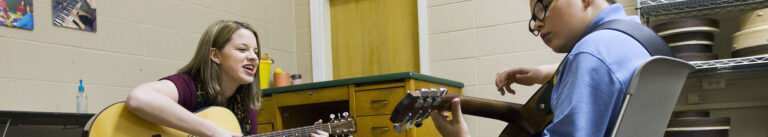 Student teaching guitar to a young boy.