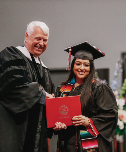 Drury University President handing a graduating senior their diploma on stage.